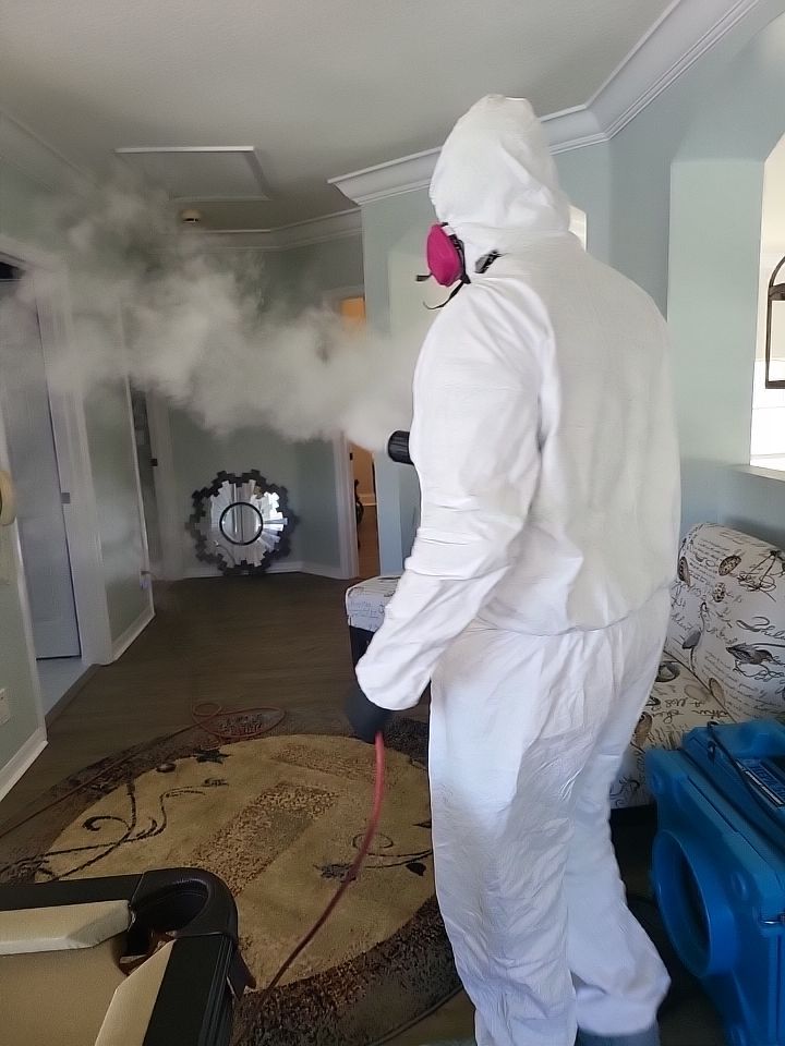 Technician in full PPE thermal fogging hallway and living room for smoke odor removal